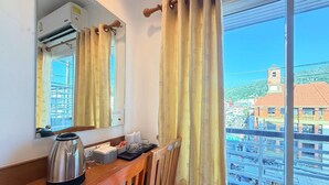 A room with a wooden desk, a kettle, and a mirror reflecting a cityscape. - Blue Neptuna Hotel Patong (Patong)