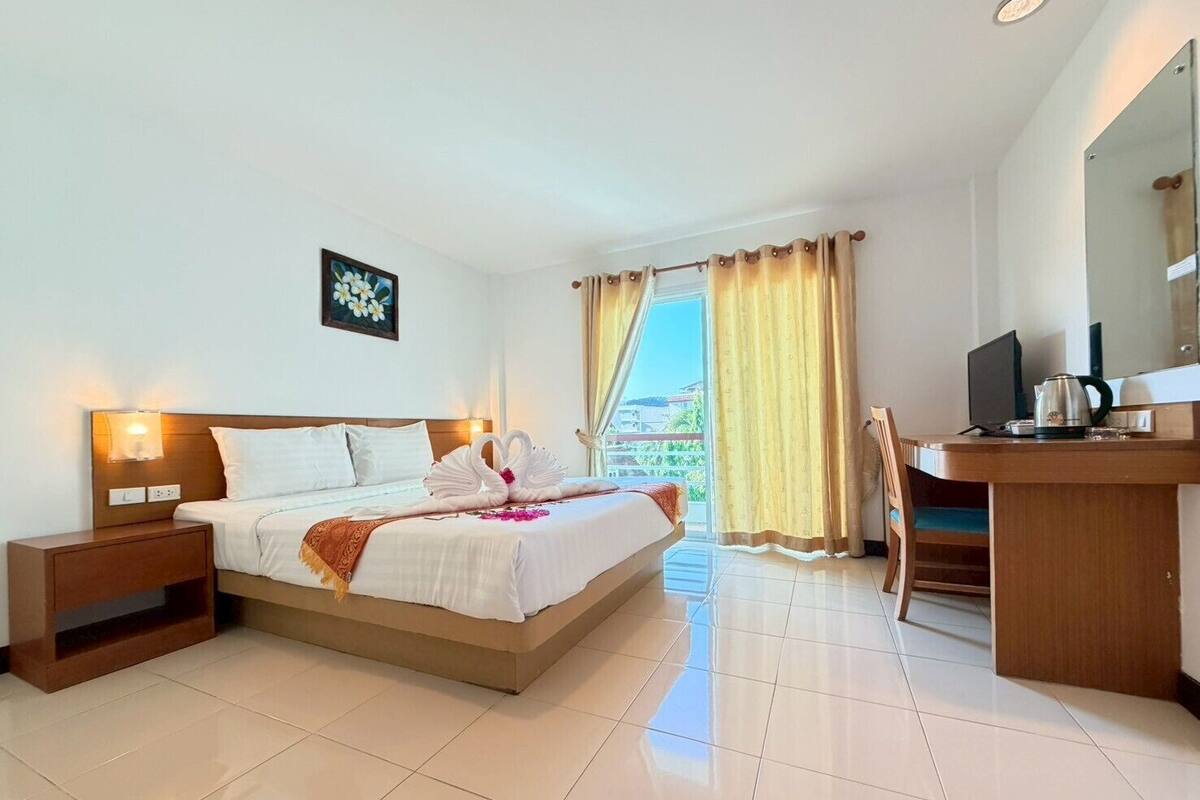Habitación de hotel con cama, mesitas de noche, un escritorio con silla, televisor y ventana con cortinas.