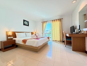 A hotel room with a bed, bedside tables, a desk with a chair, a television, and a window with curtains. - Blue Neptuna Hotel Patong (Patong)