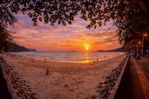 Ein Strand mit Sonnenuntergang, Menschen, die spazieren gehen, und einem Weg entlang der Küste.