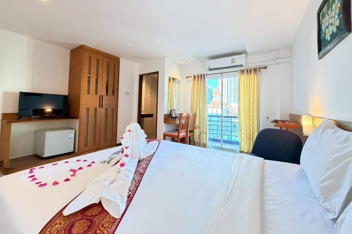 Una habitación de hotel con cama, televisión, escritorio y balcón con vista a la ciudad.