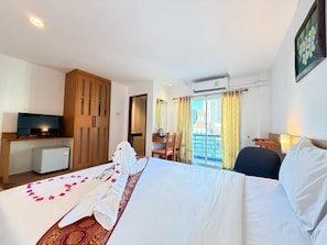 Ein Hotelzimmer mit Bett, Fernseher, Schreibtisch und Balkon mit Blick auf die Stadt.