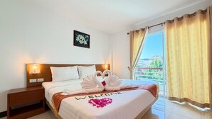 A hotel room with a bed, a nightstand, a wall-mounted light, a window with curtains, and a balcony view. - Blue Neptuna Hotel Patong (Patong)