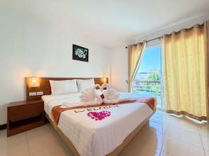 A hotel room with a bed, a nightstand, a wall-mounted light, a window with curtains, and a balcony view. - Blue Neptuna Hotel Patong (Patong)