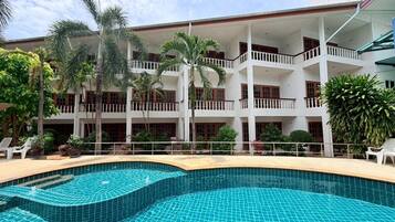 Un hotel con piscina, varios balcones y plantas tropicales.