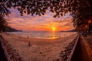 Une plage au coucher du soleil, des gens qui se promènent et un sentier qui longe le rivage.