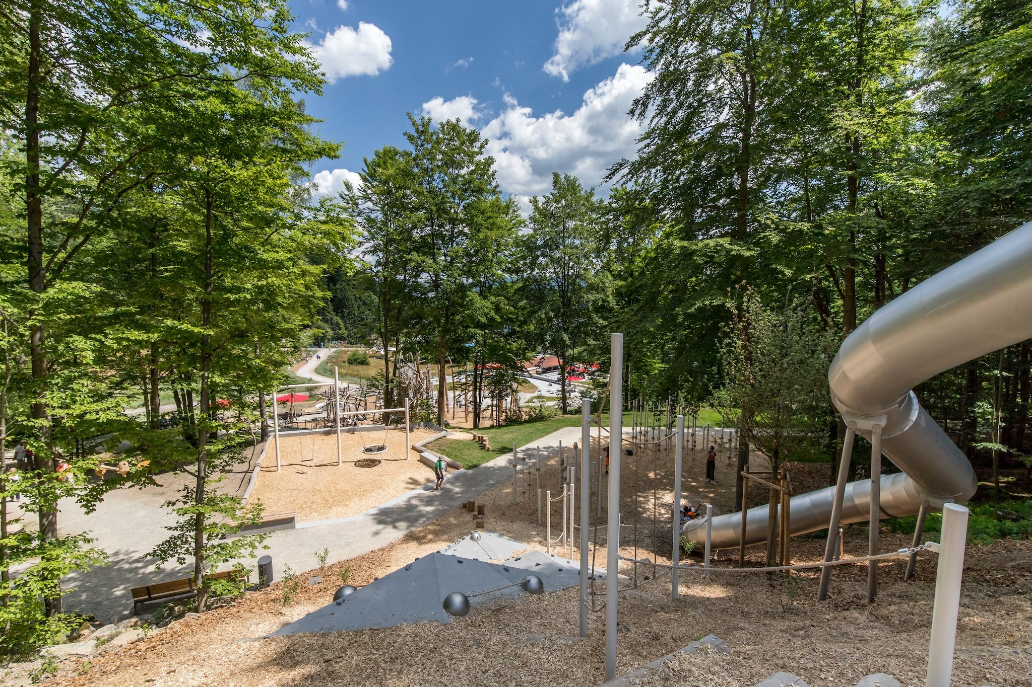 A playground with a slide, swings, and a climbing structure surrounded by trees.