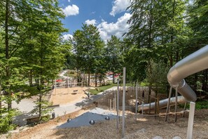 A playground with a slide, swings, and a climbing structure surrounded by trees. - Studio Robert mit Pool und Sauna (Freyung)