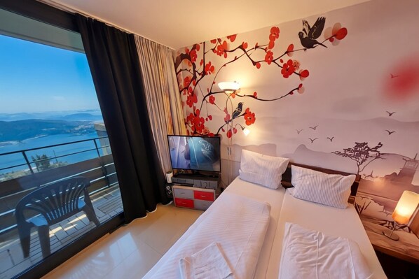 A hotel room with a balcony, a bed, a television, and a wall mural. - Studio Rainer mit Pool und Sauna (Freyung)