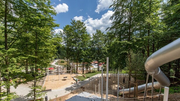 Ein Spielplatz mit Rutschen und Klettergerüsten, umgeben von Bäumen.