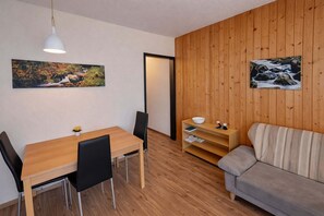 A room with a wooden floor, a dining table with chairs, a sofa, a white pendant light, and two paintings on the walls. - Studio Sebastian mit Pool und Sauna (Freyung)