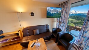 Een woonkamer met een bank, fauteuils, een salontafel, een televisie en uitzicht op bergen.