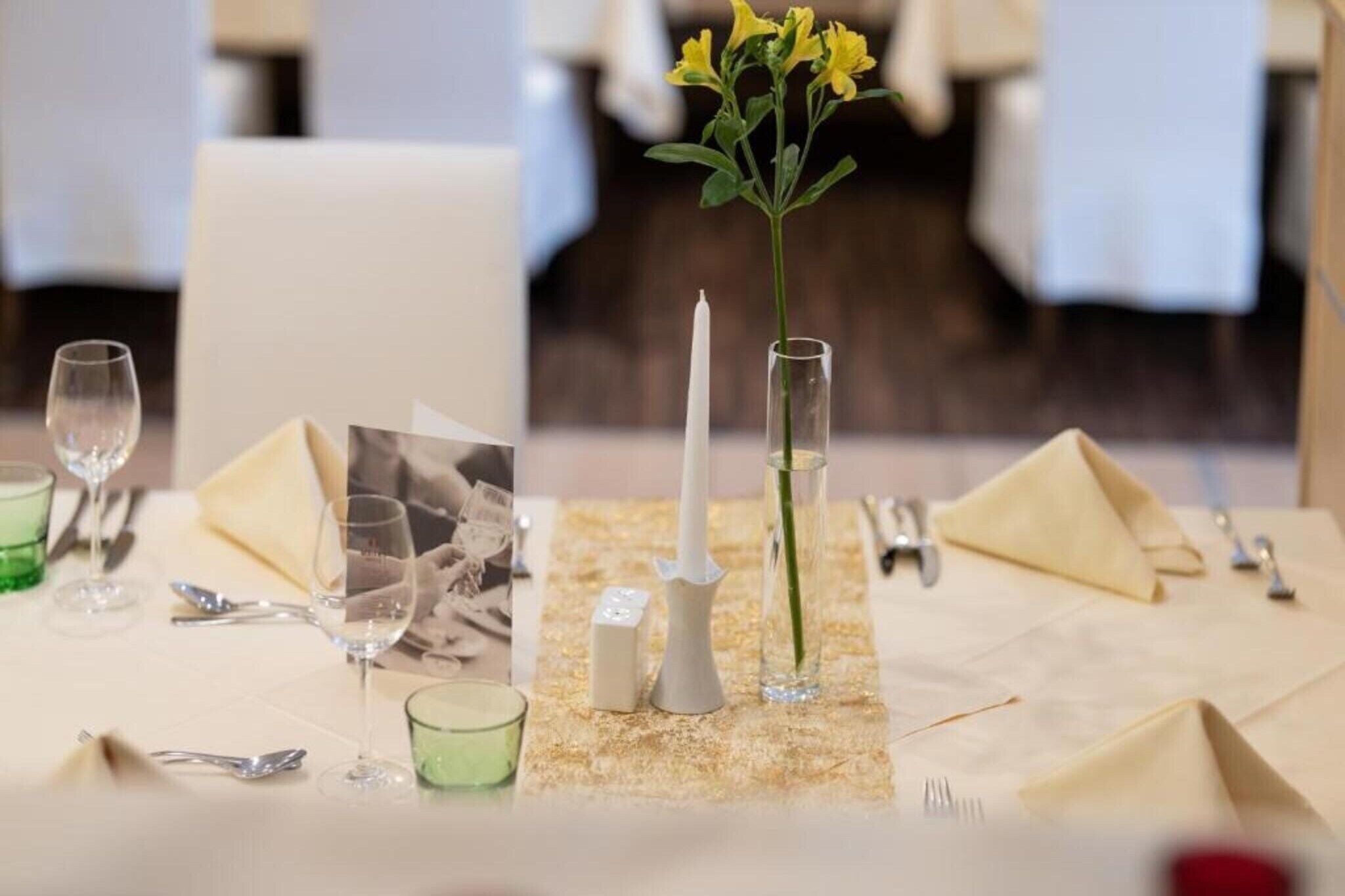 Een gedekte tafel met een kaars, een vaas met bloemen en een gevouwen servet.