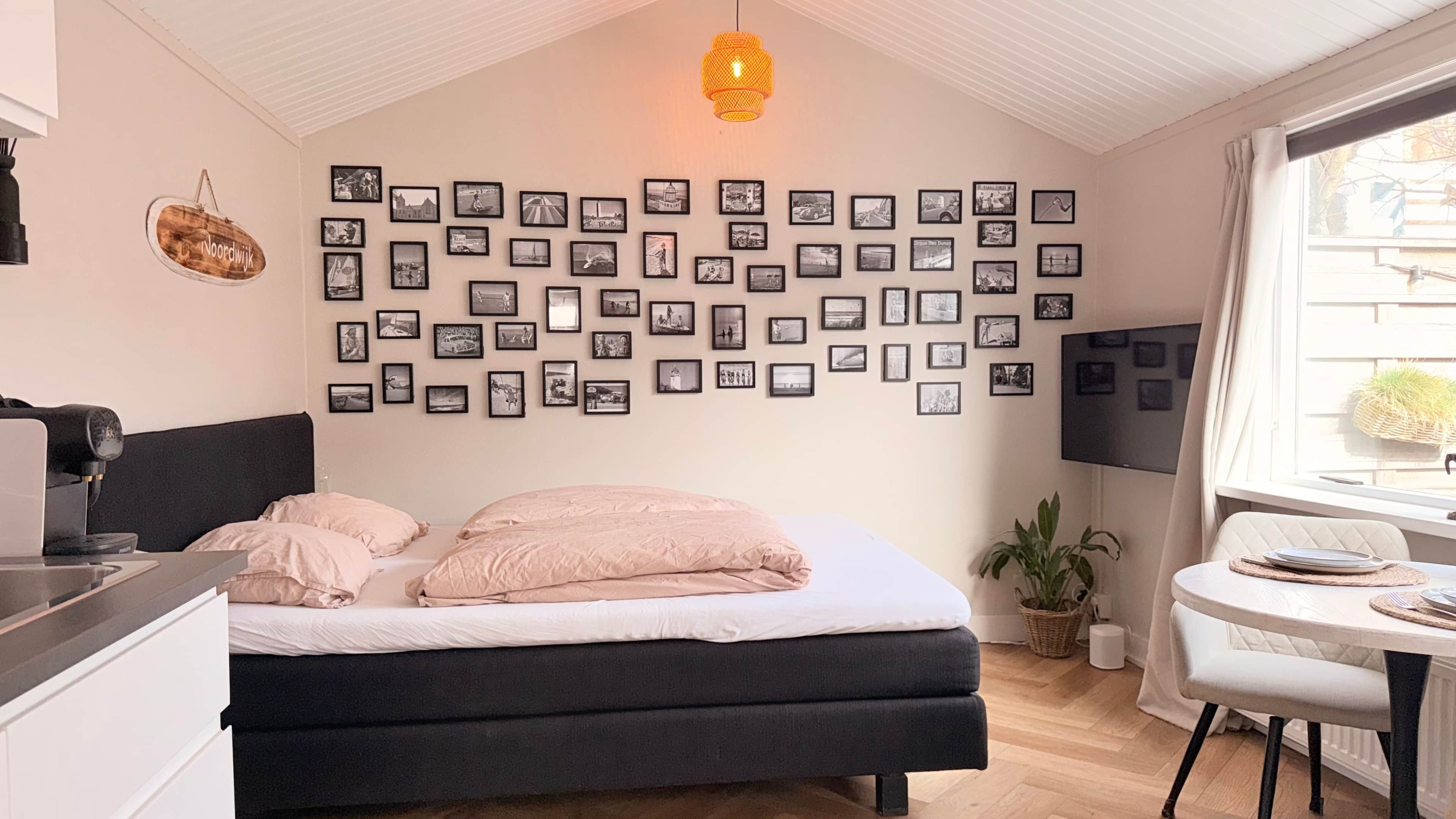 Een slaapkamer met een bed, een koffiezetapparaat, een televisie en een muur met ingelijste foto's.