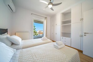 A bedroom with two beds, a ceiling fan, a radiator, and a large wardrobe. - Elenis Sea & The City Apartment, Apartment (Rethymno)