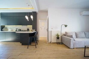 A modern kitchen with a central island, a dining area with chairs, a sofa, and a radiator. - Elenis Sea & The City Apartment, Apartment (Rethymno)