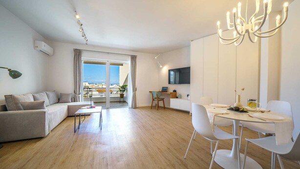 Sala moderna com sofá, mesa de jantar, cadeiras, TV na parede e varanda com vista.
