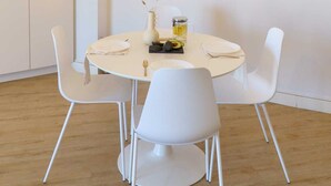 Uma sala de jantar com uma mesa redonda, cadeiras brancas, um lustre moderno e decoração minimalista.