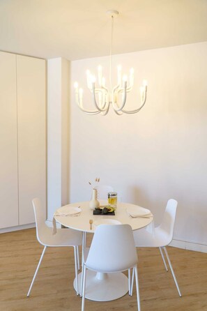 A dining area with a round table, white chairs, a modern chandelier, and a minimalist decor. - Elenis Sea & The City Apartment, Apartment (Rethymno)