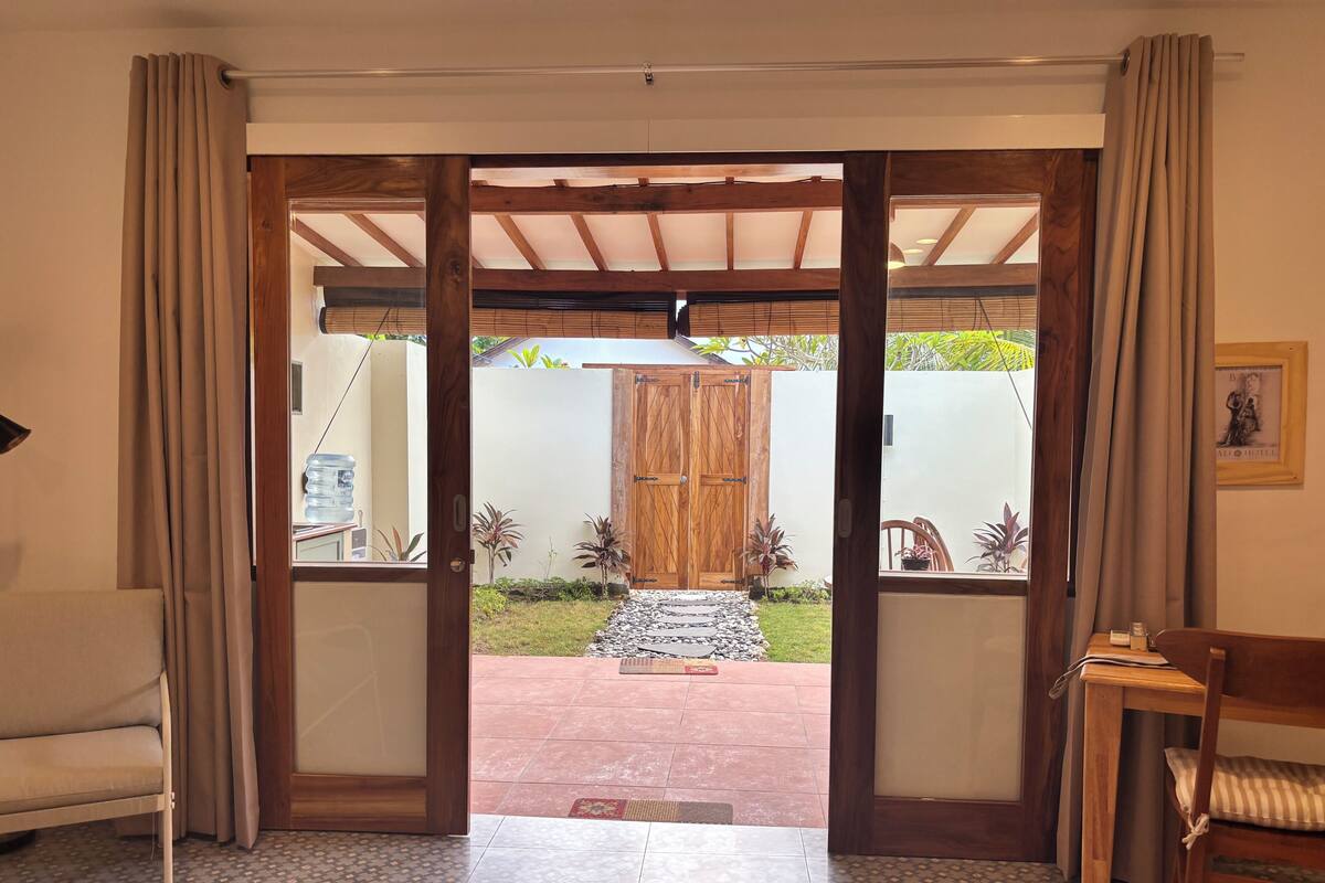 Un umbral abierto que da a un patio con una puerta de madera, un banco y un suelo de baldosas.