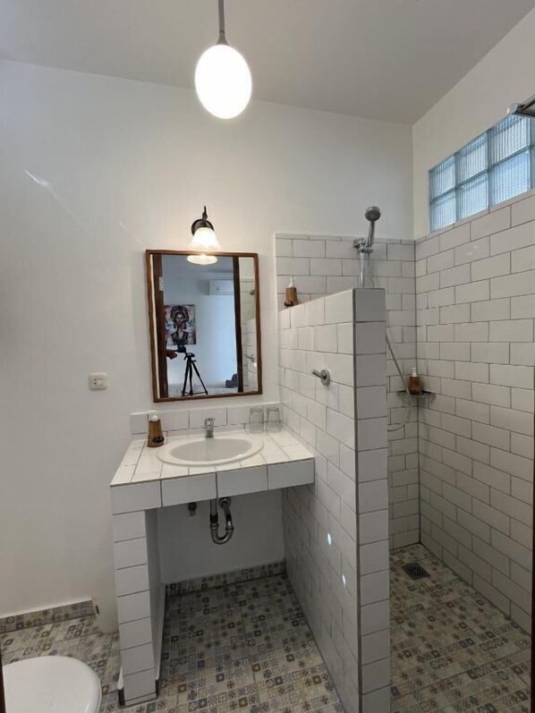 A bathroom with a white sink, mirror, and shower. - Living Room Lembongan (Lembongan Island)