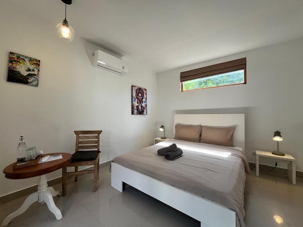 A bedroom with a bed, a chair, a small table, a lamp, and artwork on the walls.
