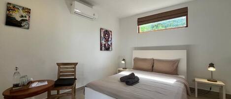 A bedroom with a bed, a chair, a small table, a lamp, and artwork on the walls.