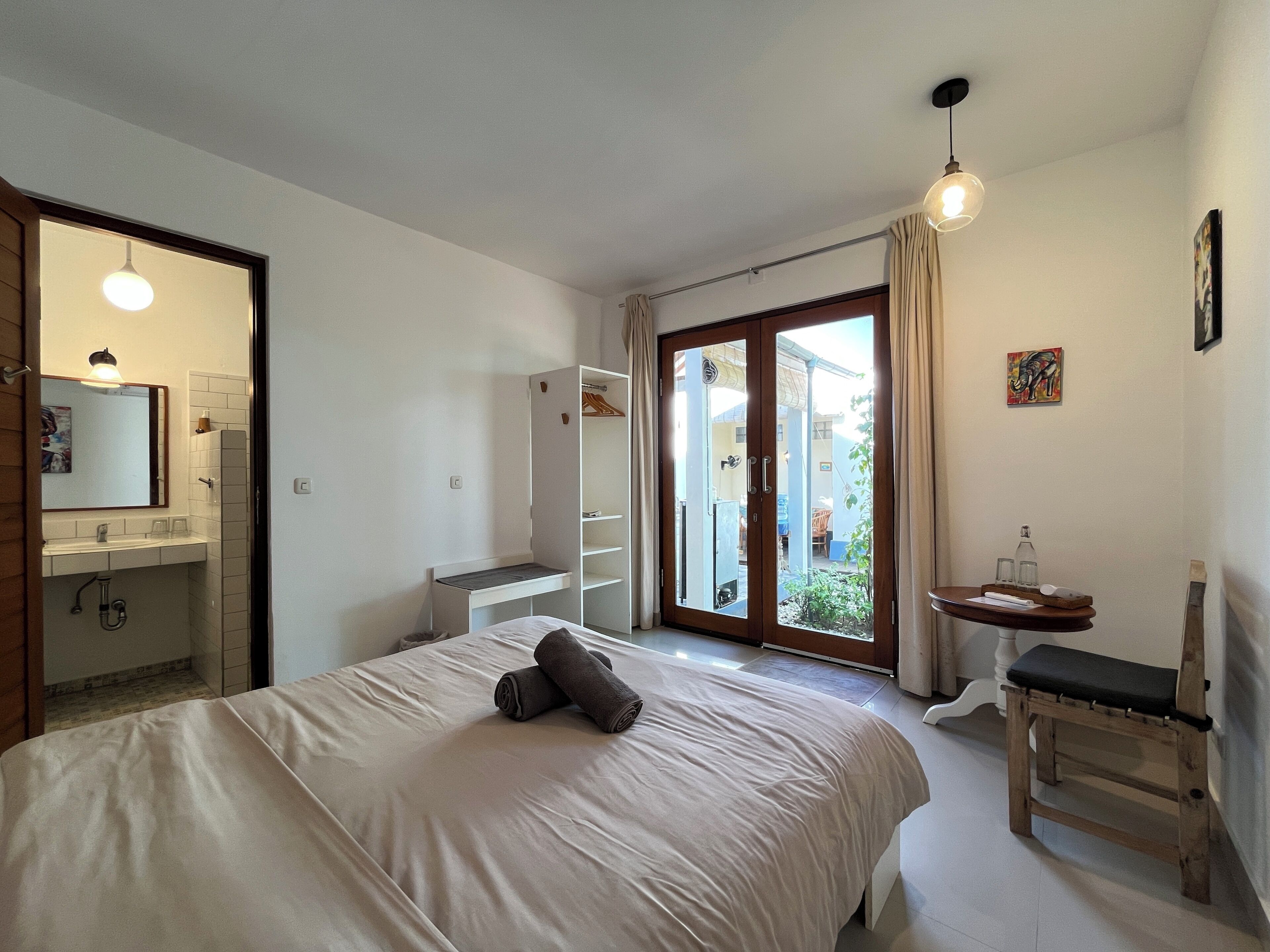 A bedroom with a bed, a bedside table, a wardrobe, a bathroom, and a view of the outside.