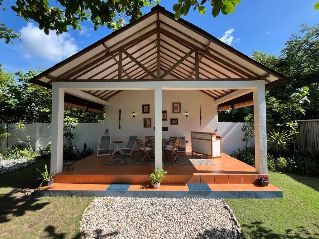 Un espacio de estar al aire libre cubierto con una mesa y sillas, rodeado de un jardín.