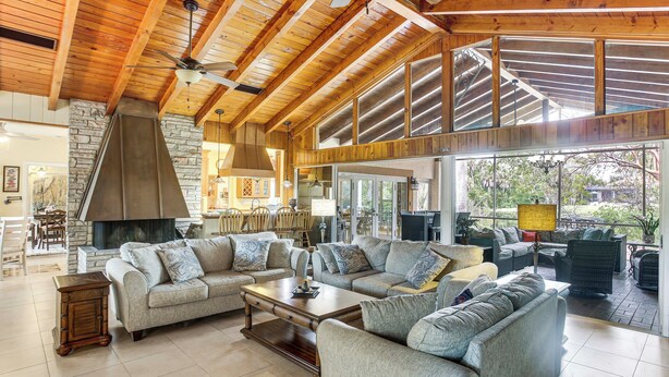 A spacious living room with a high ceiling, stone wall, and large windows. - Private Pool & Dock: Riverfront 'Bridge Escape' (North Fort Myers)