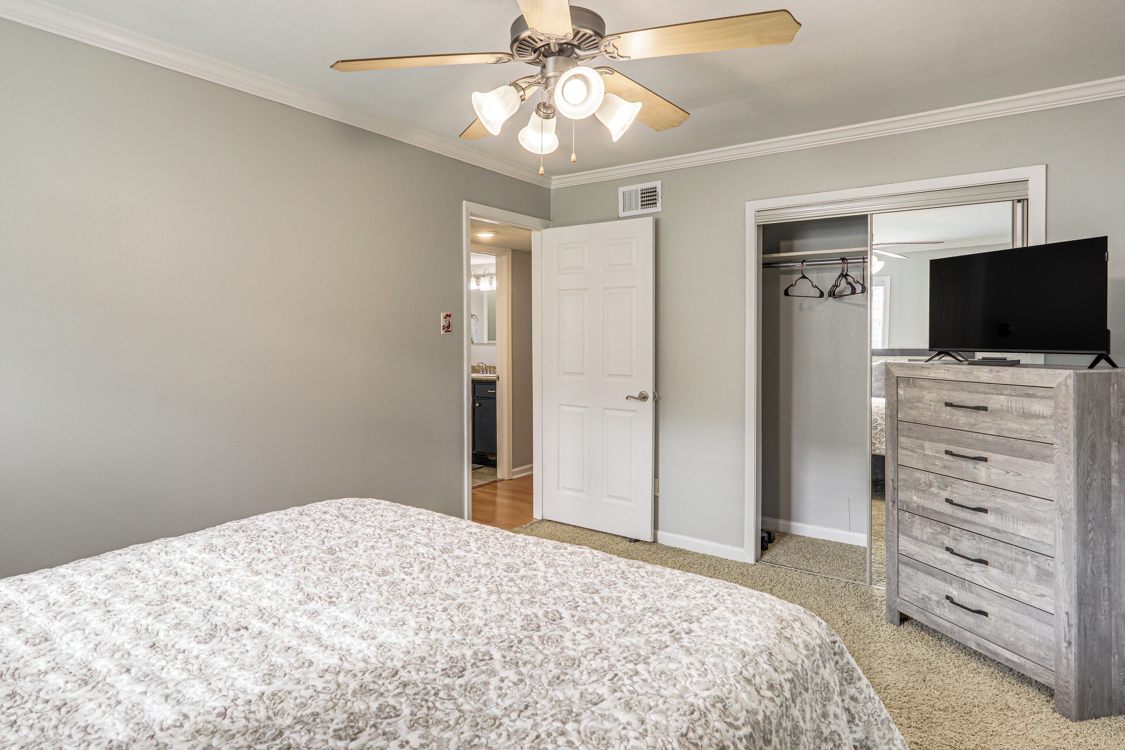 Une chambre à coucher avec un lit, un ventilateur de plafond, une commode et un téléviseur.
