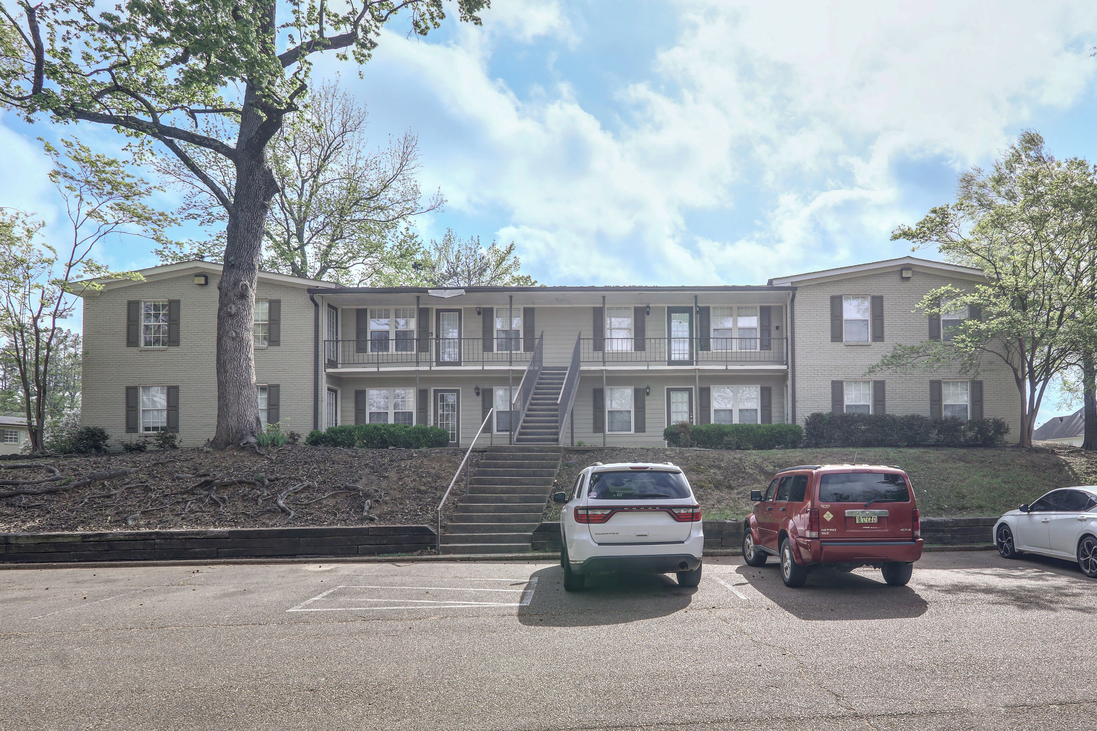 A multi-story building with a parking lot, a staircase, and a tree.