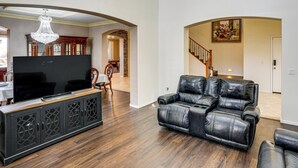 A living room with a flat-screen TV, leather recliner, wooden cabinet, chandelier, and a staircase. - Swim-Up Bar & Games! Ultimate Goodyear Group Stay (Goodyear)