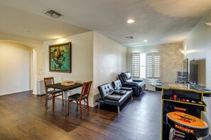 A living room with a dining table, chairs, a sofa, and a gaming table.