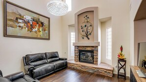 A living room with a fireplace, leather sofa, and a chandelier. - Swim-Up Bar & Games! Ultimate Goodyear Group Stay (Goodyear)