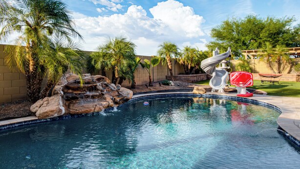 A swimming pool with a rock waterfall, palm trees, and a slide. - Swim-Up Bar & Games! Ultimate Goodyear Group Stay (Goodyear)