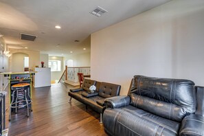 A living room with a leather sofa, a bar area with stools, and a staircase leading to another level.