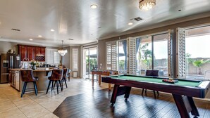 A spacious living area with a pool table, a kitchen with a bar, and large windows offering a view of the outdoors. - Swim-Up Bar & Games! Ultimate Goodyear Group Stay (Goodyear)