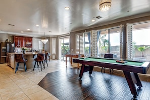 Een ruime woonkamer met een pooltafel, een keuken met een bar en grote ramen met uitzicht op de omgeving.