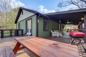 Um deck de madeira com uma mesa de piquenique, churrasqueira e área de estar coberta com ventilador de teto.
