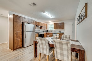 A modern kitchen with wooden cabinets, a stainless steel refrigerator, and a dining area with checkered chairs and a table set for two.