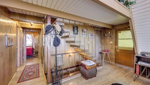 Interior de madeira com escada, uma mesa pequena e uma porta.