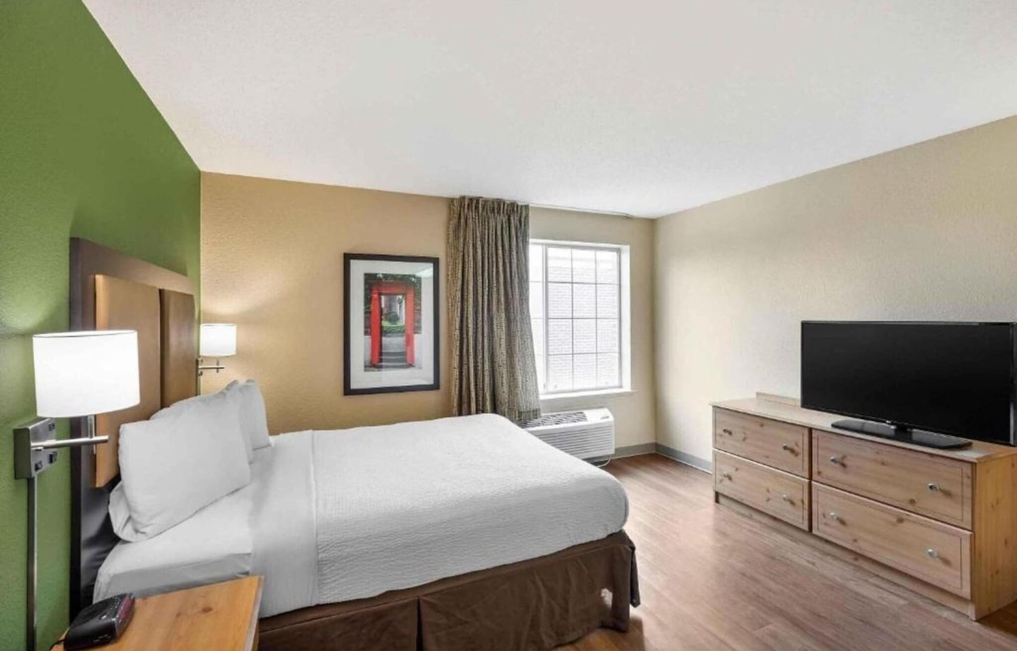 A hotel room with a bed, a television, a dresser, and a framed picture on the wall.