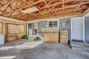 A covered outdoor area with a concrete floor, wooden benches, a small table, and a door.