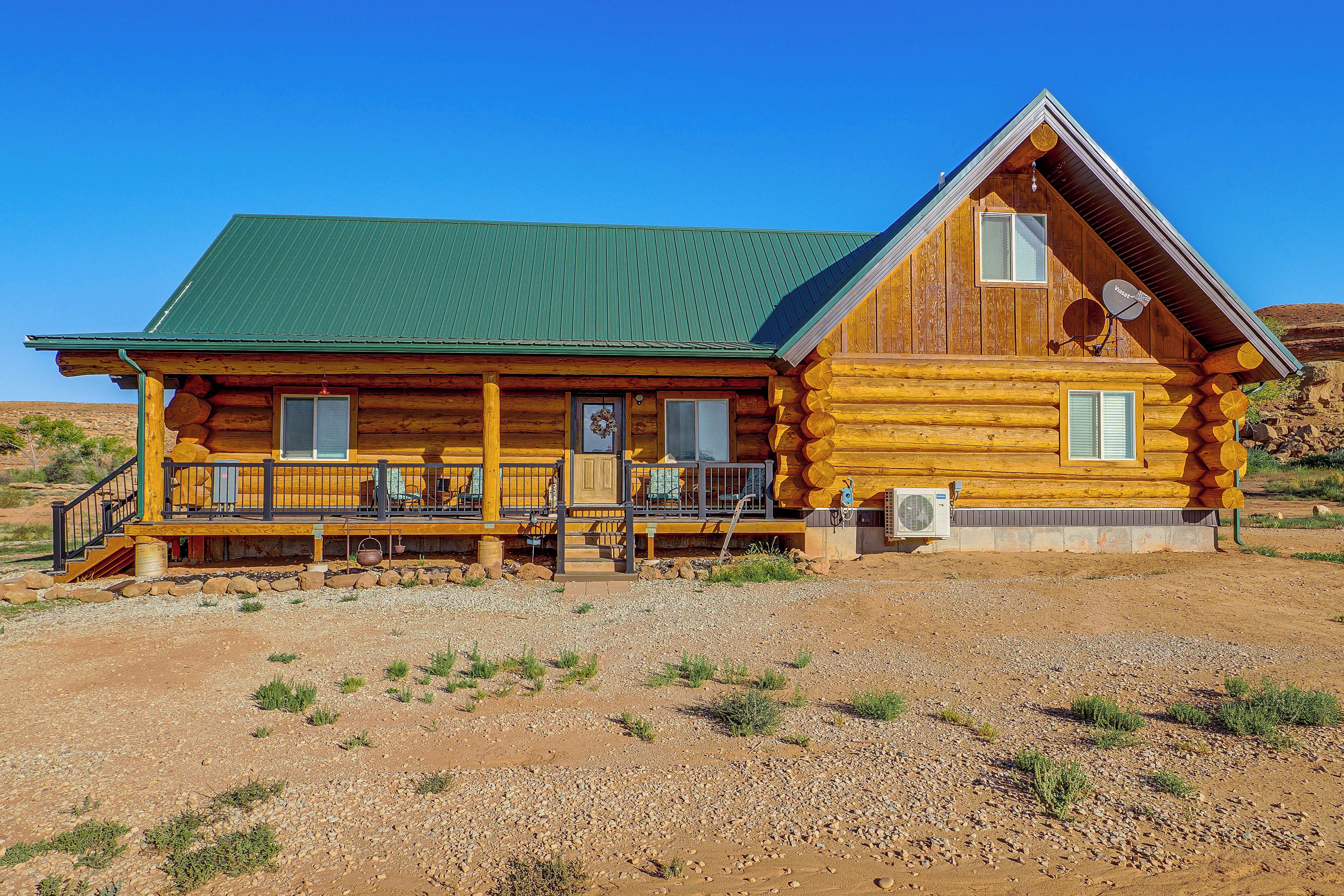 A log cabin with a green roof, a porch with seating, and a satellite dish.