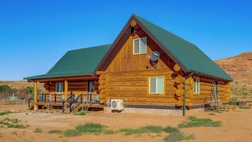 A log cabin with a porch, a satellite dish, and an air conditioning unit.