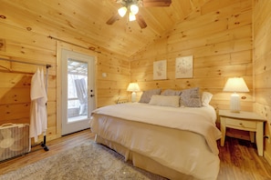 Quarto de cabana de madeira com uma cama, duas luminárias de cabeceira, uma porta e uma pequena mesa.