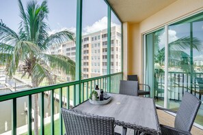 A balcony with wicker furniture, a table with a tray, and a view of a building and palm trees. - Sunsets & Sails! Waterfront Punta Gorda Condo (Punta Gorda)