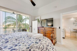 A bedroom with a bed, a dresser, a television, and a balcony with palm trees. - Sunsets & Sails! Waterfront Punta Gorda Condo (Punta Gorda)