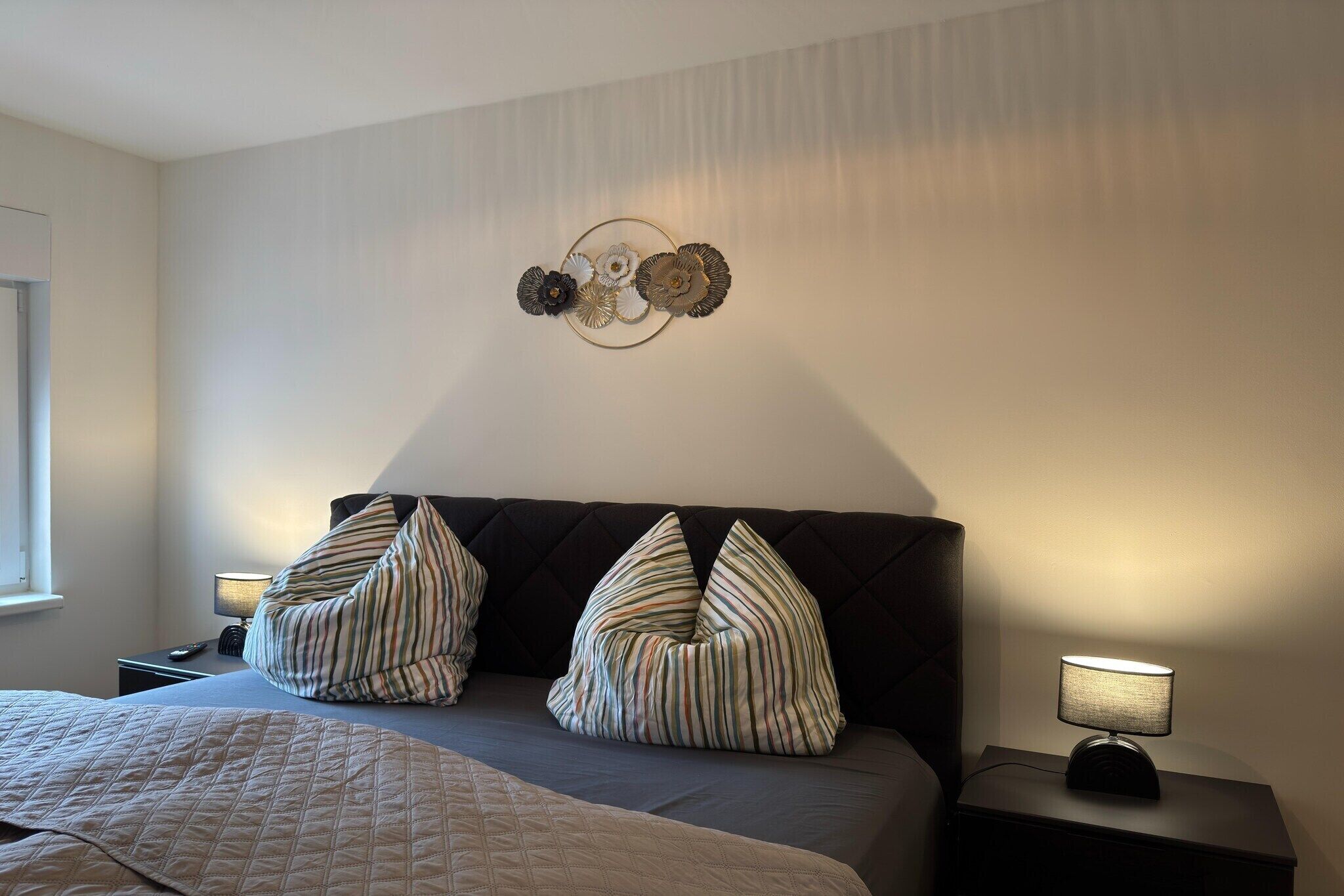 Ein Schlafzimmer mit einem Bett, zwei Kissen, einem Nachttisch mit Lampe und einer Wanddekoration.